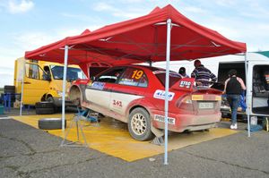 A red rally car having maintenance under a tent