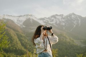 A woman using binoculars, standing in a mountain landscape